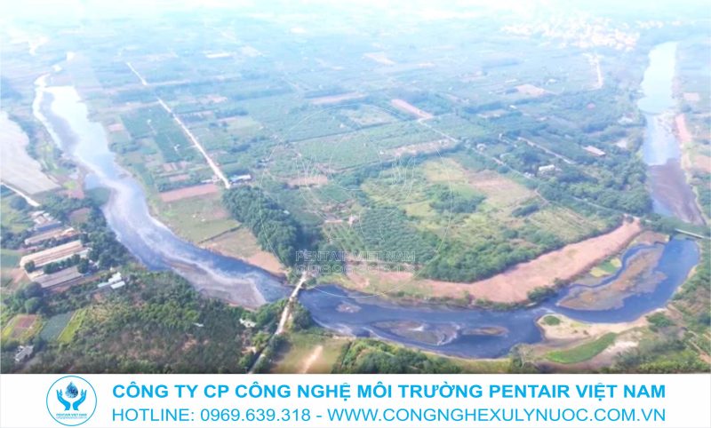 Hình ảnh dòng sông Đáy nhìn từ trên cao với mặt nước màu đen đậm do ô nhiễm, tương phản với bờ sông đang được cải tạo.